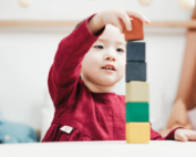 Young child in a red dress stacking colorful blocks at Early Achievers Preschool in Hawaii, fostering creativity and development.