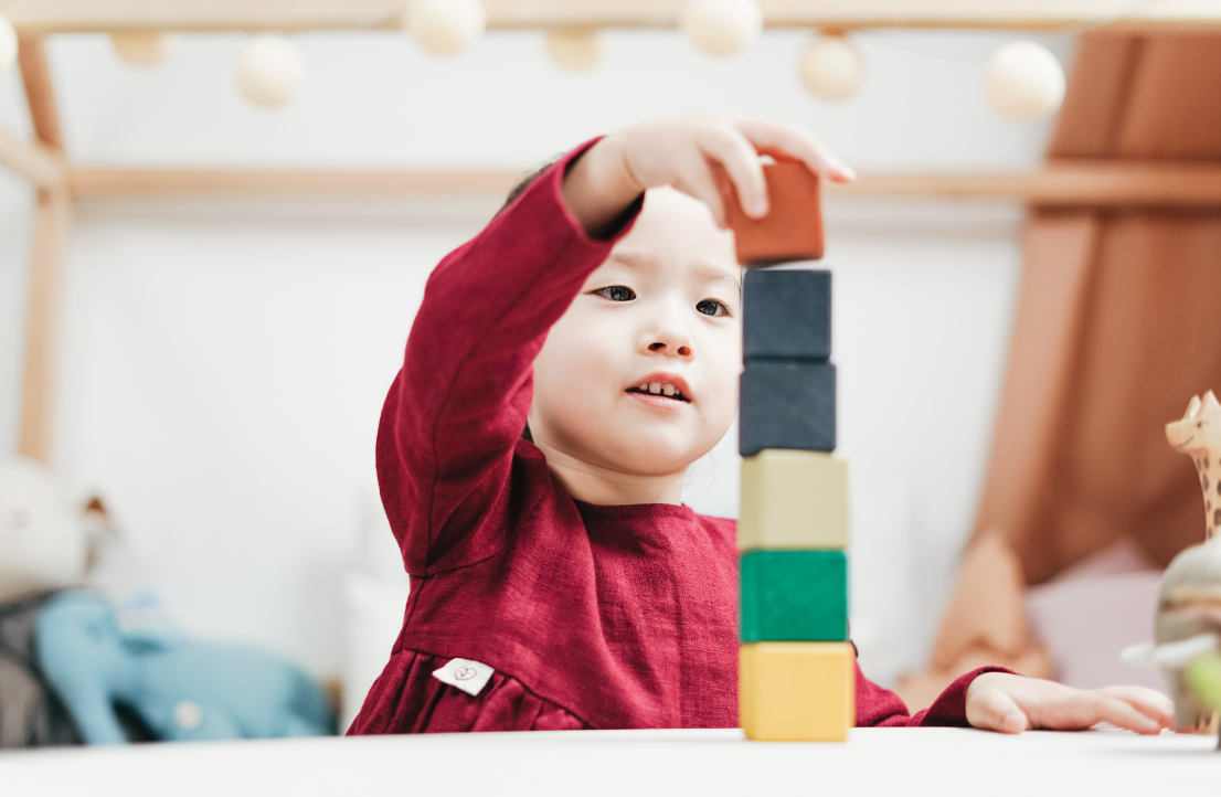 Preschool student in red sweater stacking colorful building blocks during early childhood development activities at Early Achievers