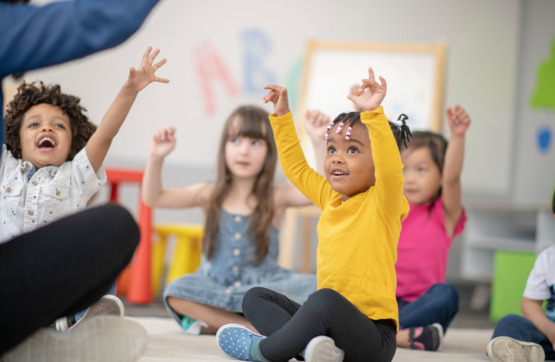 Diverse group of preschool children engaged in interactive learning activities, raising hands enthusiastically during circle time