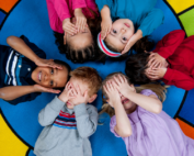 Diverse group of children playing peekaboo on colorful rug at Early Achievers Preschool Hawaii.