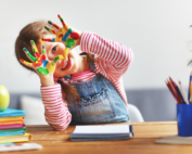 Smiling preschool girl with painted hands at Early Achievers Preschool Hawaii, showcasing creativity through hands-on art activities.