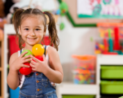 Preschool girl smiling and holding colorful balls, promoting communication and sharing at Early Achievers Preschool Hawaii