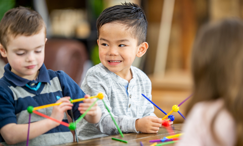 Early Achievers Preschool Hawaii STEM activity with preschooler smiling while building colorful shapes, hands-on learning and early education