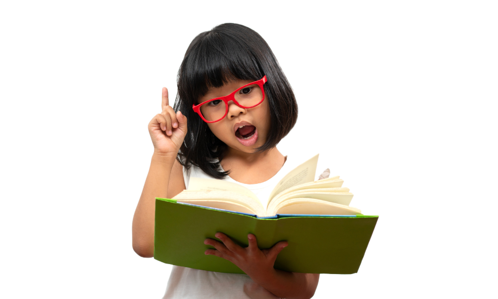 Young girl with red glasses reading a book and raising her finger, representing learning and curiosity at Early Achievers Preschool Hawaii