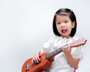 Early Achievers Preschool Hawaii child playing a small guitar, supporting music and movement learning through creative, hands-on play.